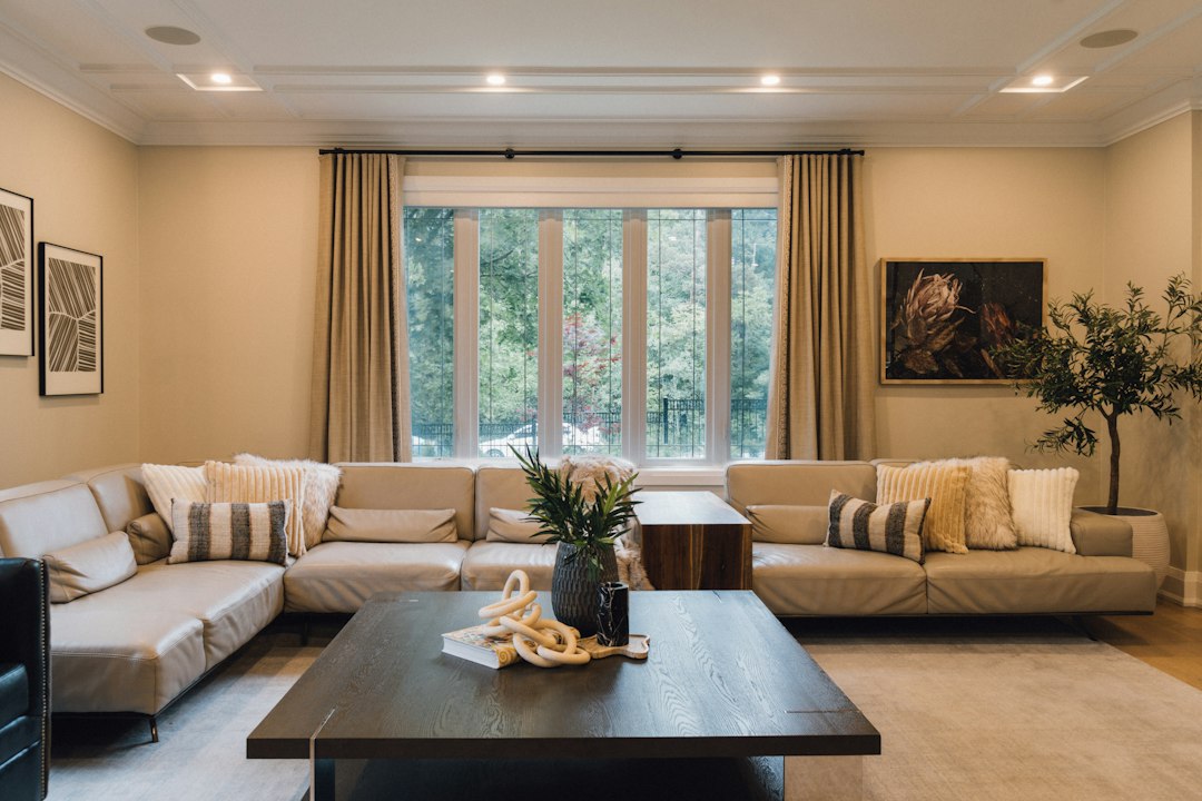 Comfortable living room with beige sofas, a dark coffee table, and windows facing trees