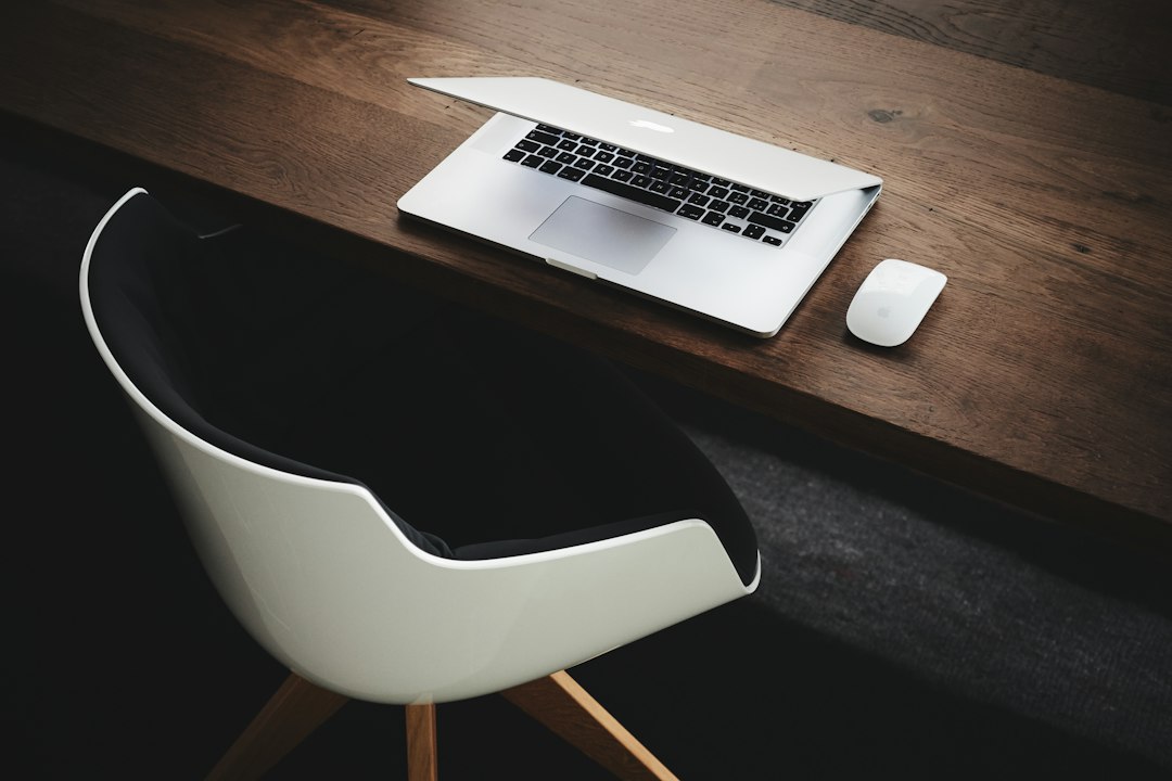 Laptop and white mouse on a wooden desk with a white chair