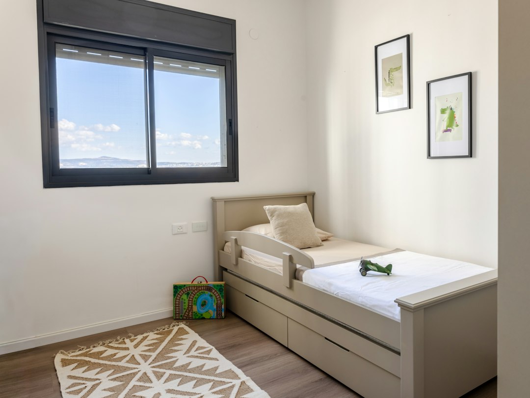 Small white bed and toys beneath a bedroom window