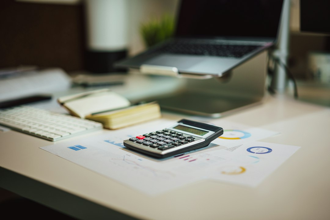 A calculator, notebook, laptop, and printed charts arranged on a desk.