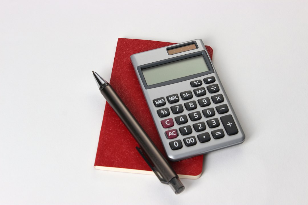 A calculator and pen resting on a red notebook.