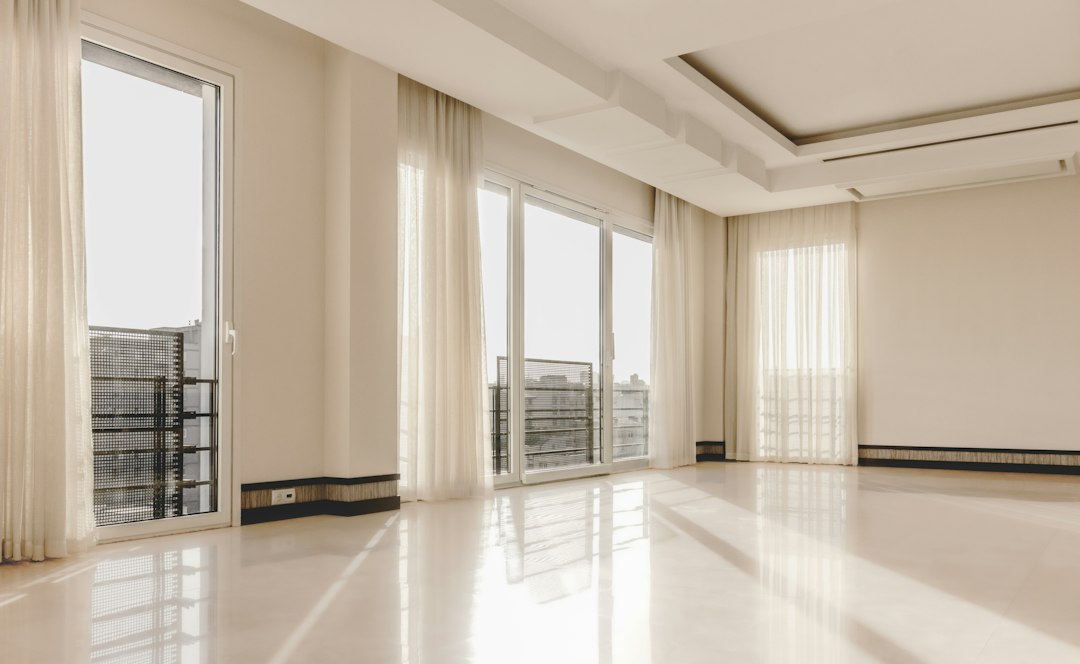 An empty living room with tall windows, curtains, and a polished tile floor.