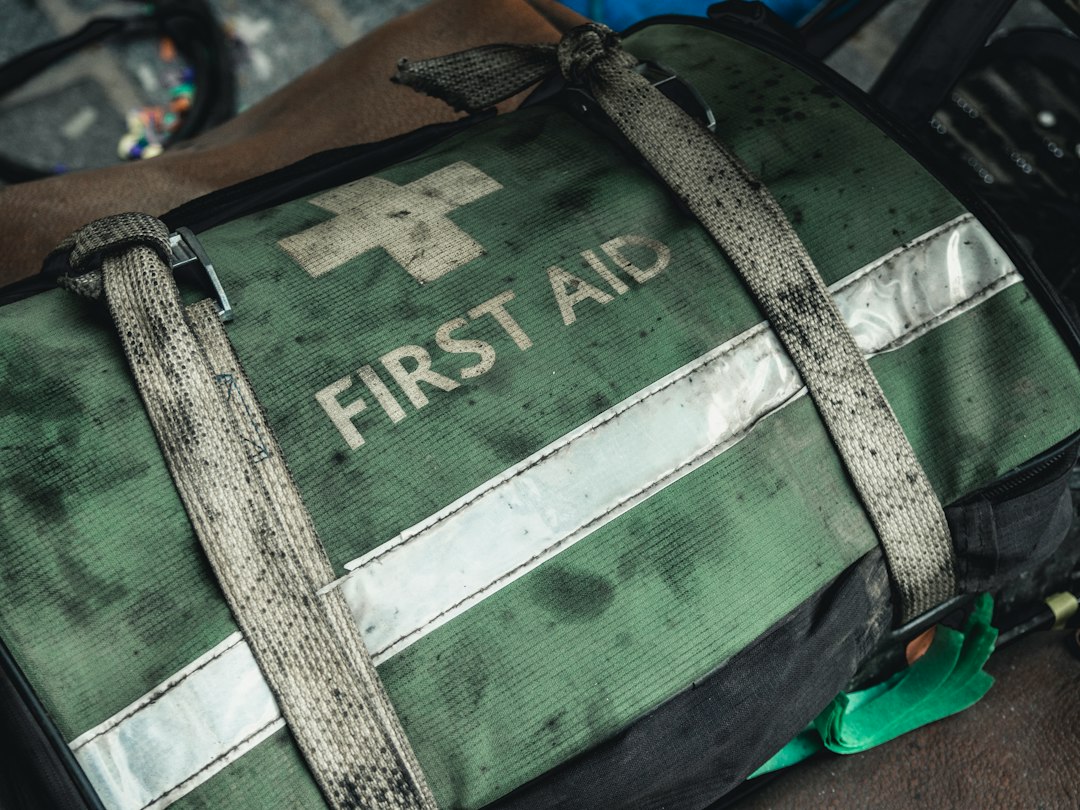 A worn green bag marked First Aid with a strap and reflective strip.