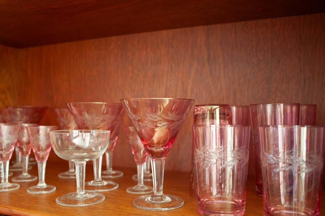 Pink and clear stemmed glasses arranged on a wooden shelf.