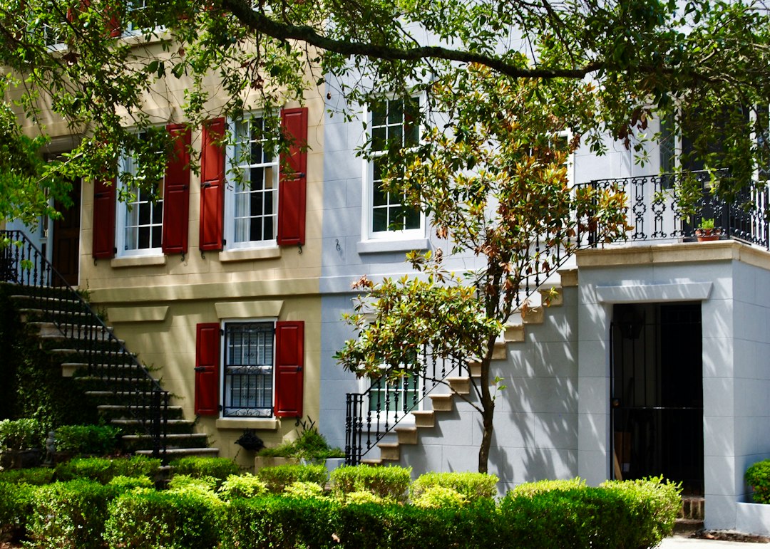 Historic townhouse facade with red shutters and twin front stairways.