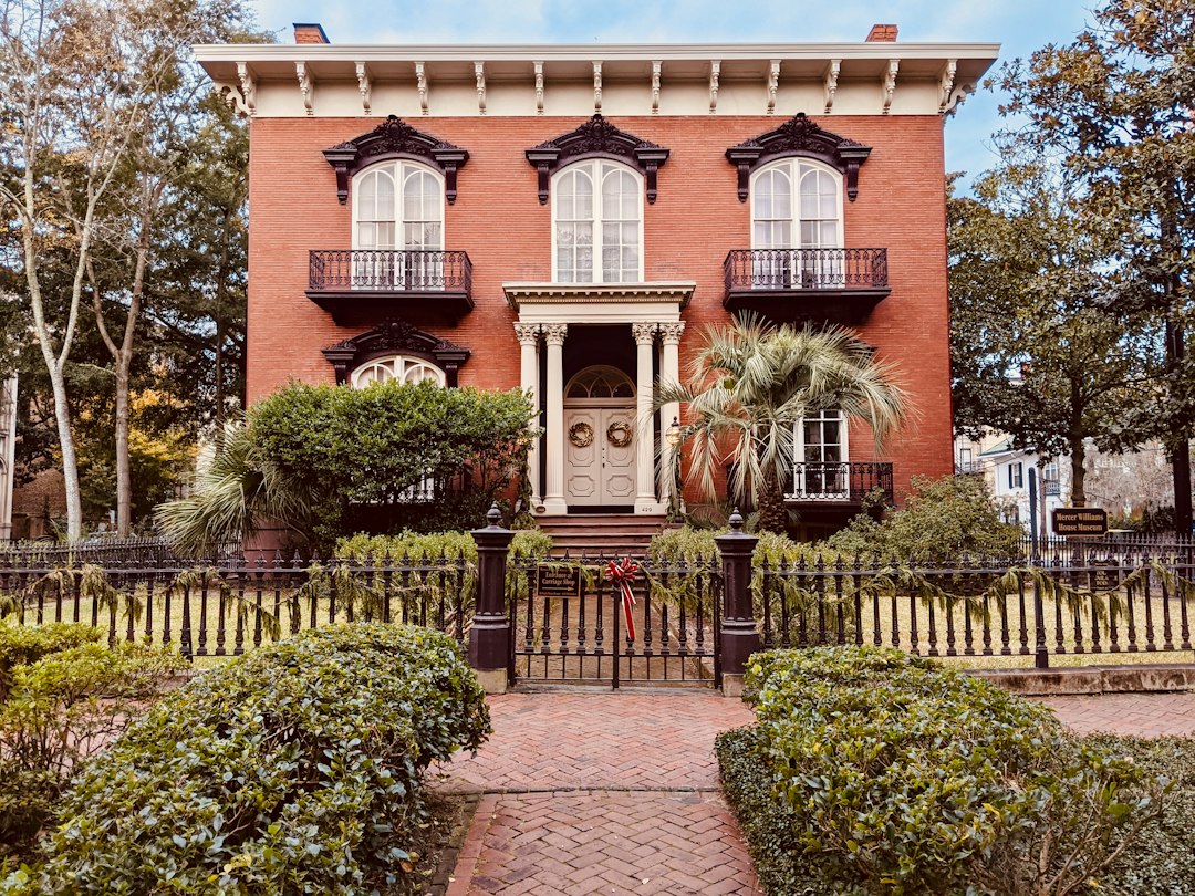 Red-brick historic house with wrought-iron fencing and a palm tree.