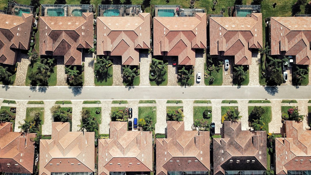 Overhead photograph of homes with terracotta roofs, palm trees, driveways, and screened pools