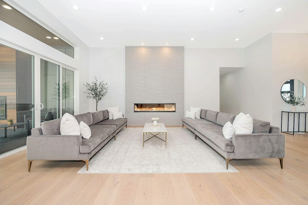 Bright living room with two gray sofas, a pale rug, and a slim fireplace