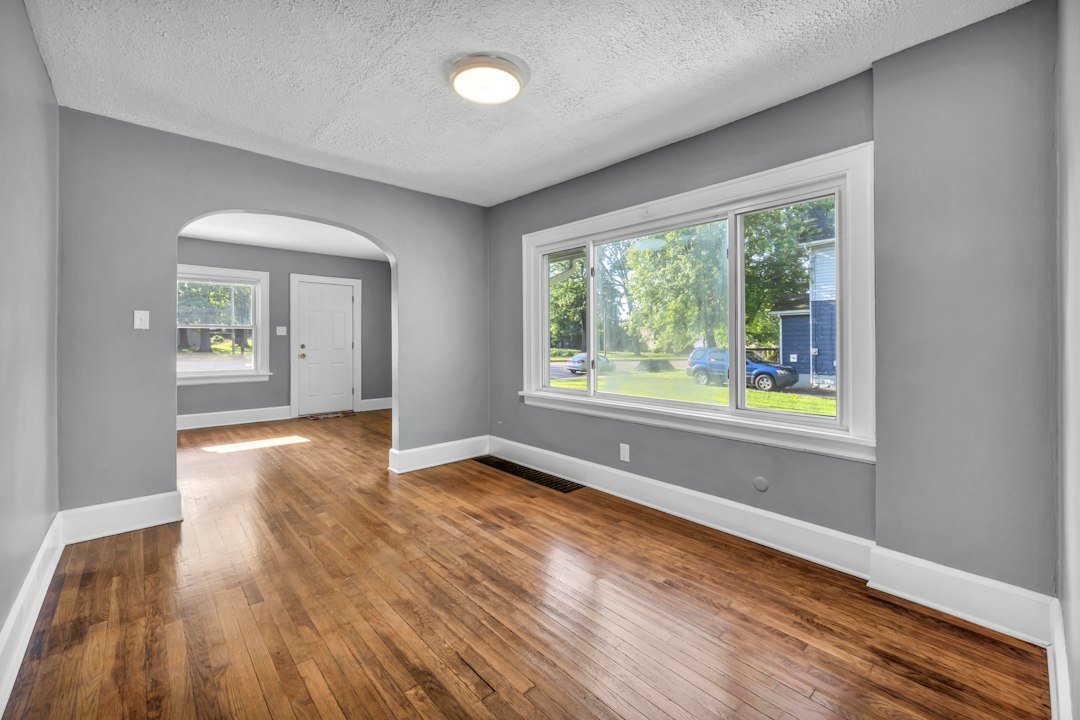 Empty living room with hardwood floors, a picture window, and an arched doorway.