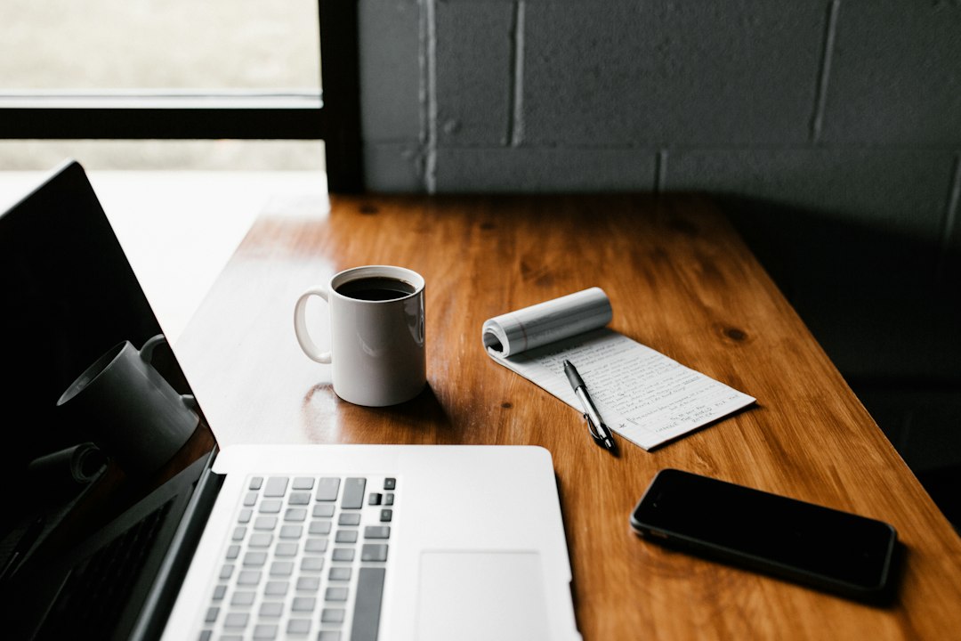 Laptop, phone, coffee mug and notepad on a wooden desk