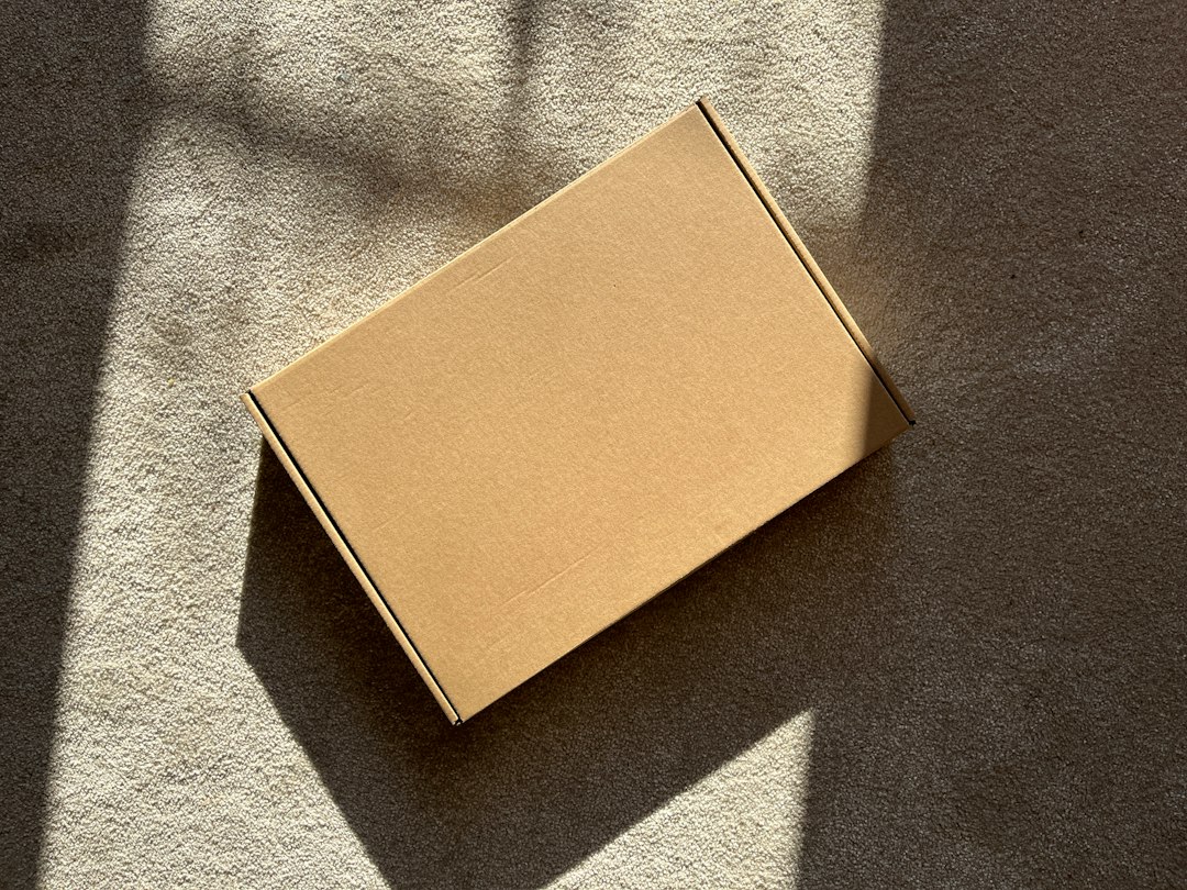 A sealed cardboard box resting on a textured surface in sunlight.