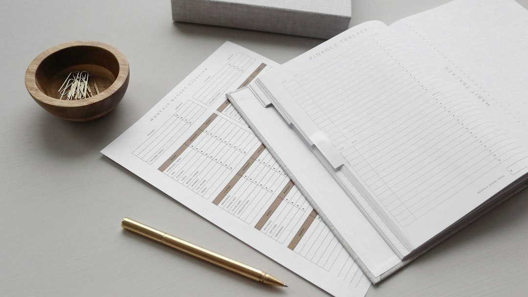Budget planner pages with a gold pen and a small bowl of paper clips.