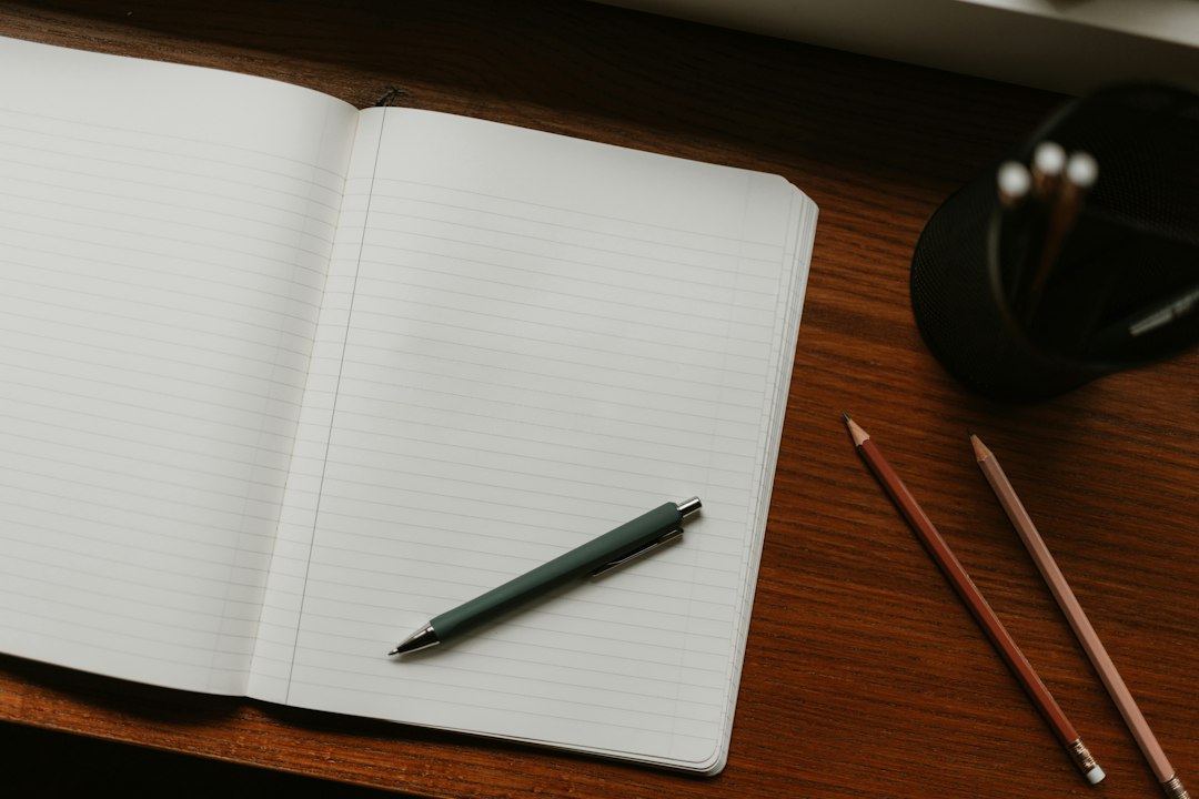 An open lined notebook with a green pen on a wooden desk.