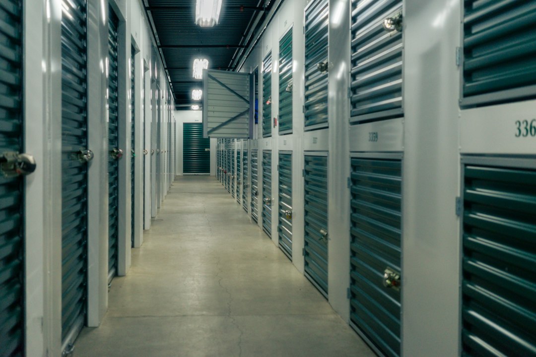 A long indoor corridor of green roll-up storage units.