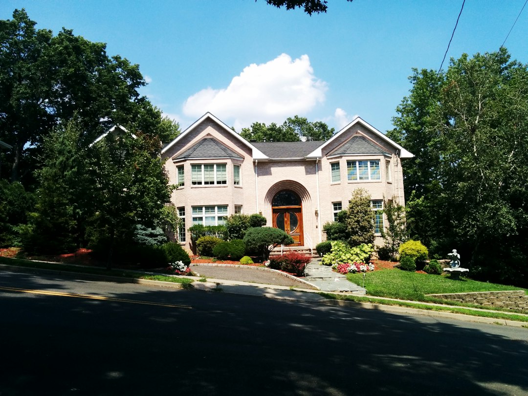 A large house with a front driveway, flowering shrubs, and mature trees.