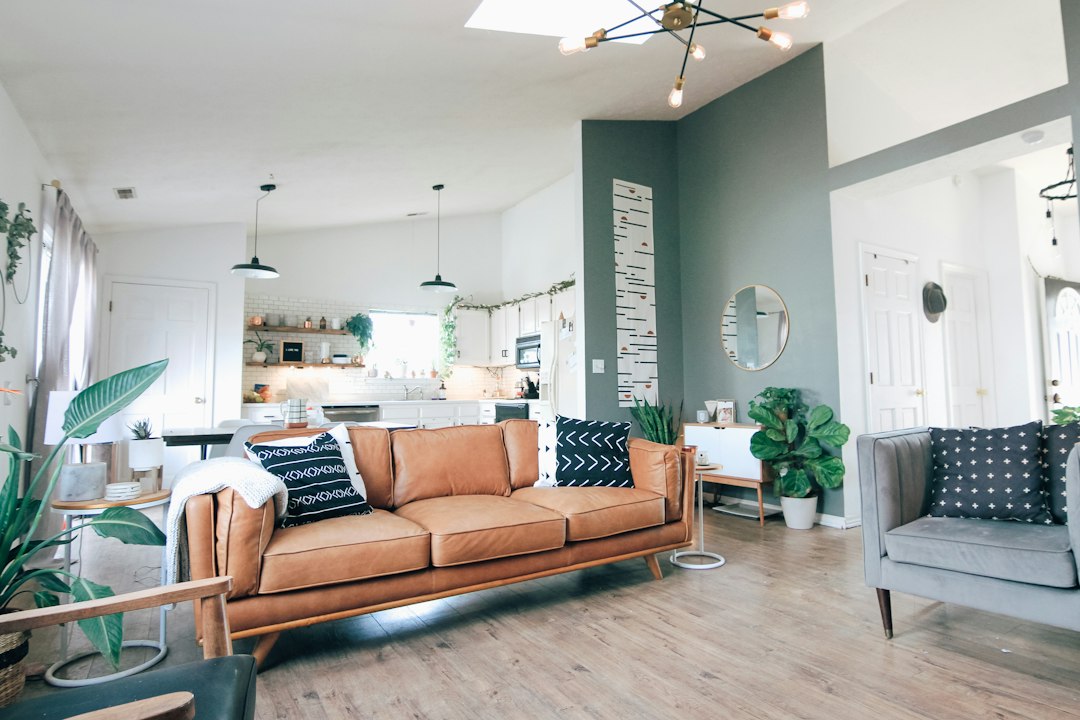 Home living room with a brown leather sofa, houseplants, and an open kitchen