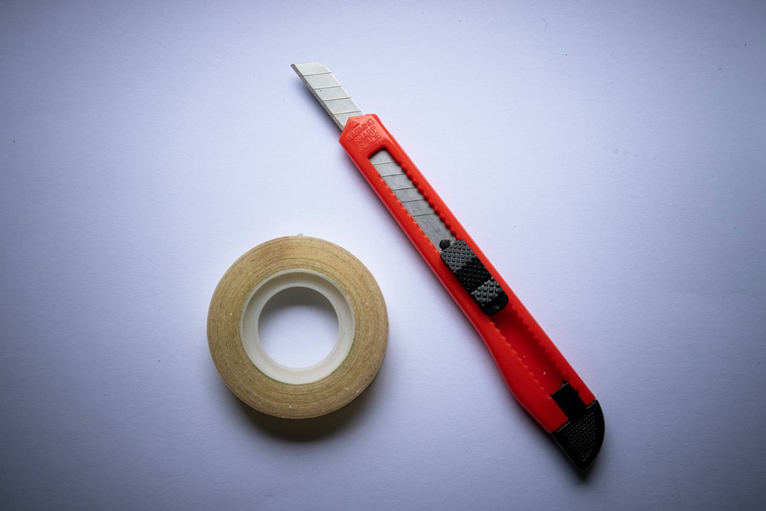 A roll of clear tape and a red utility knife on a white surface