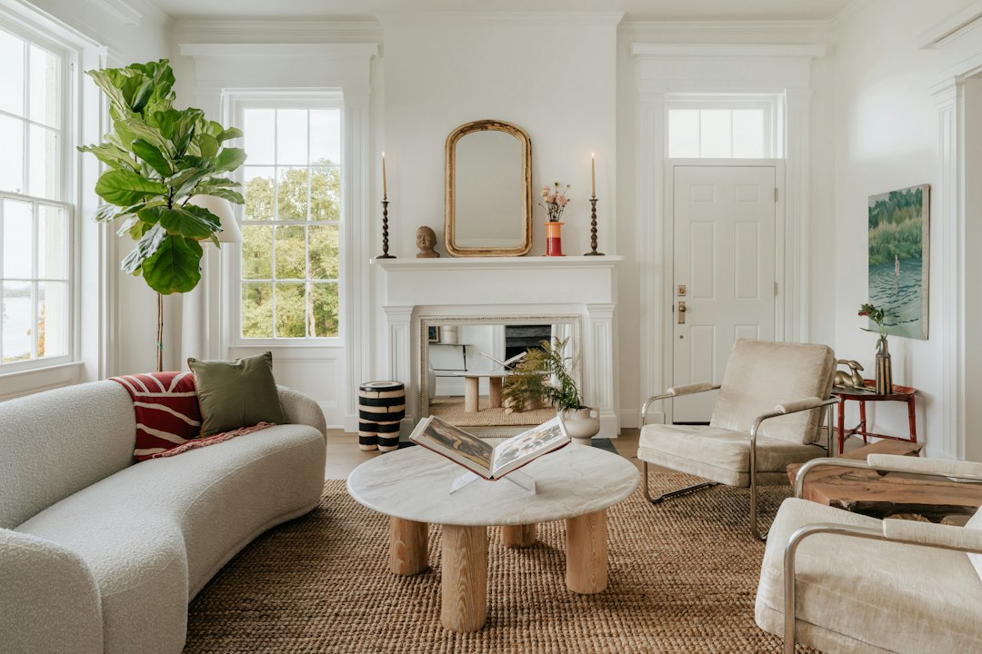 White living room with a pale sofa, fireplace, round coffee table, and leafy plants