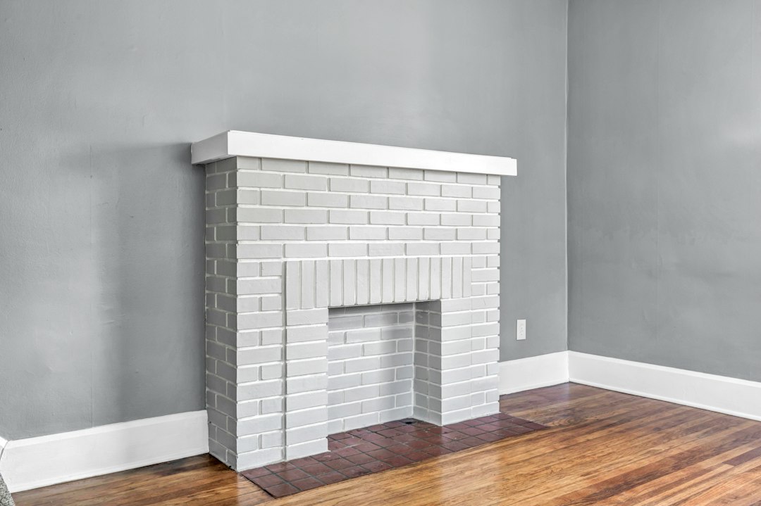 White brick fireplace against a gray wall in an empty room with hardwood floors.