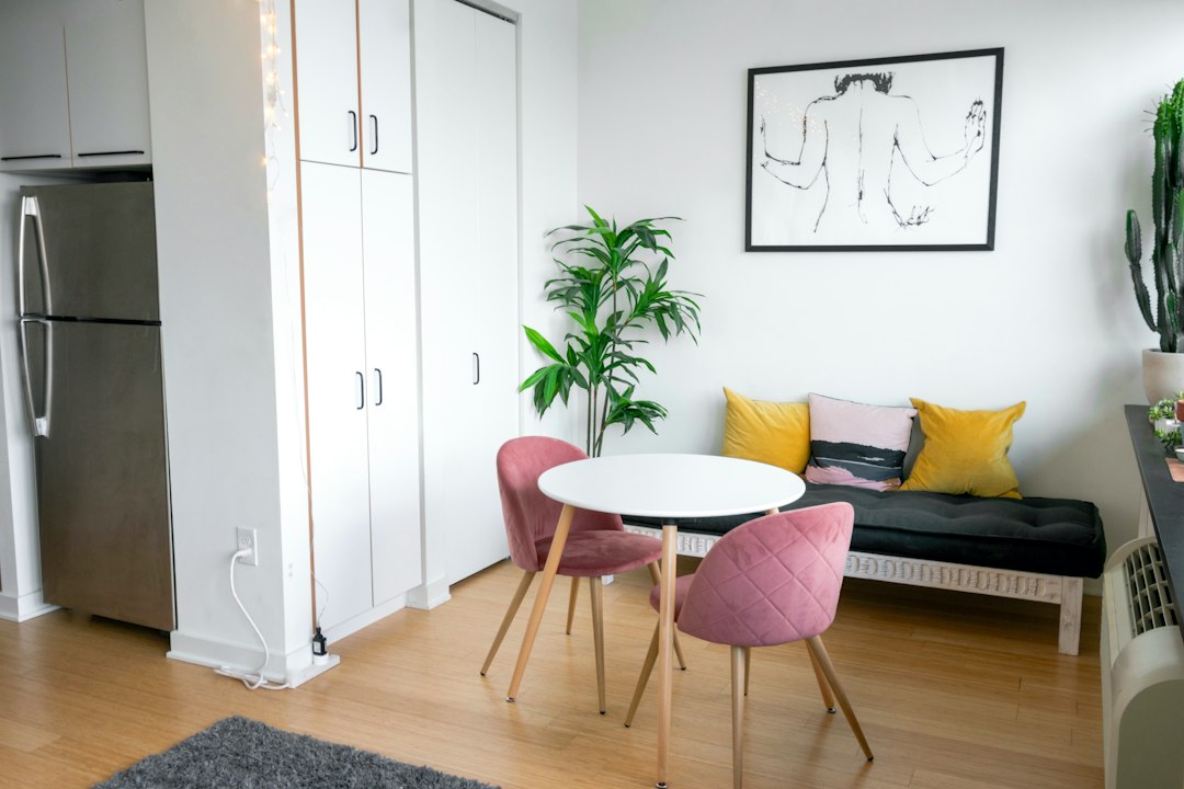 Compact apartment with a small dining table, pink chairs, and a cushioned bench.