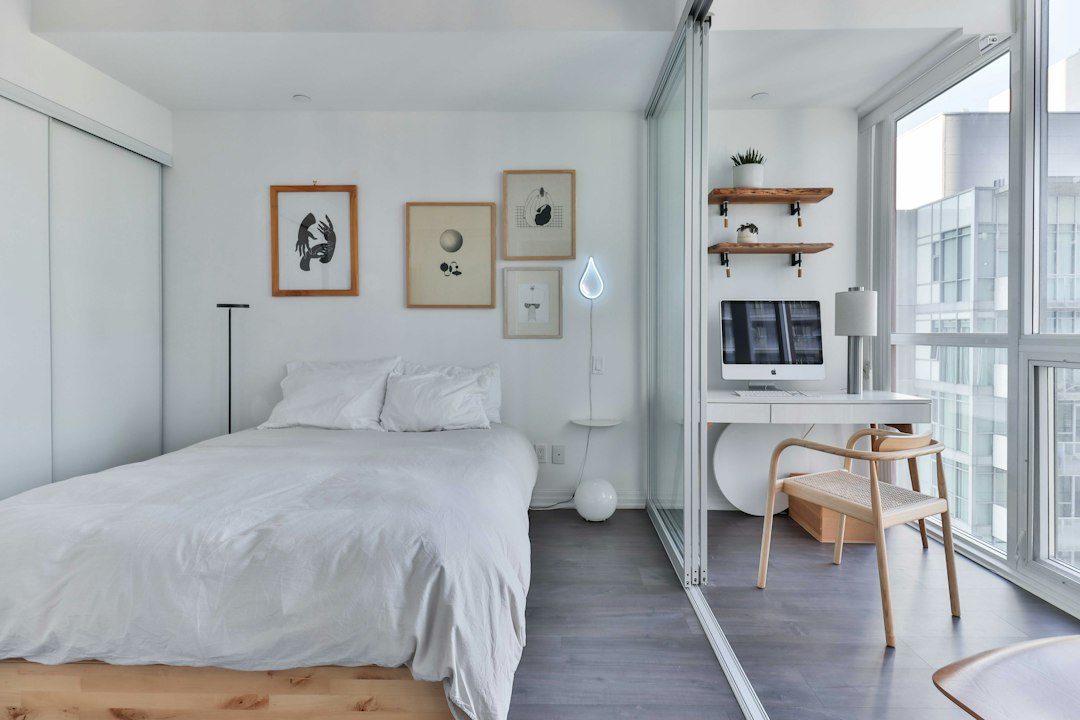 White bed beside a small desk and chair in a bright room