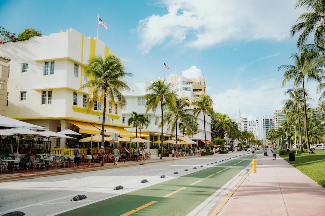 Palm-lined street with pastel buildings, outdoor seating, and a sunny sidewalk.
