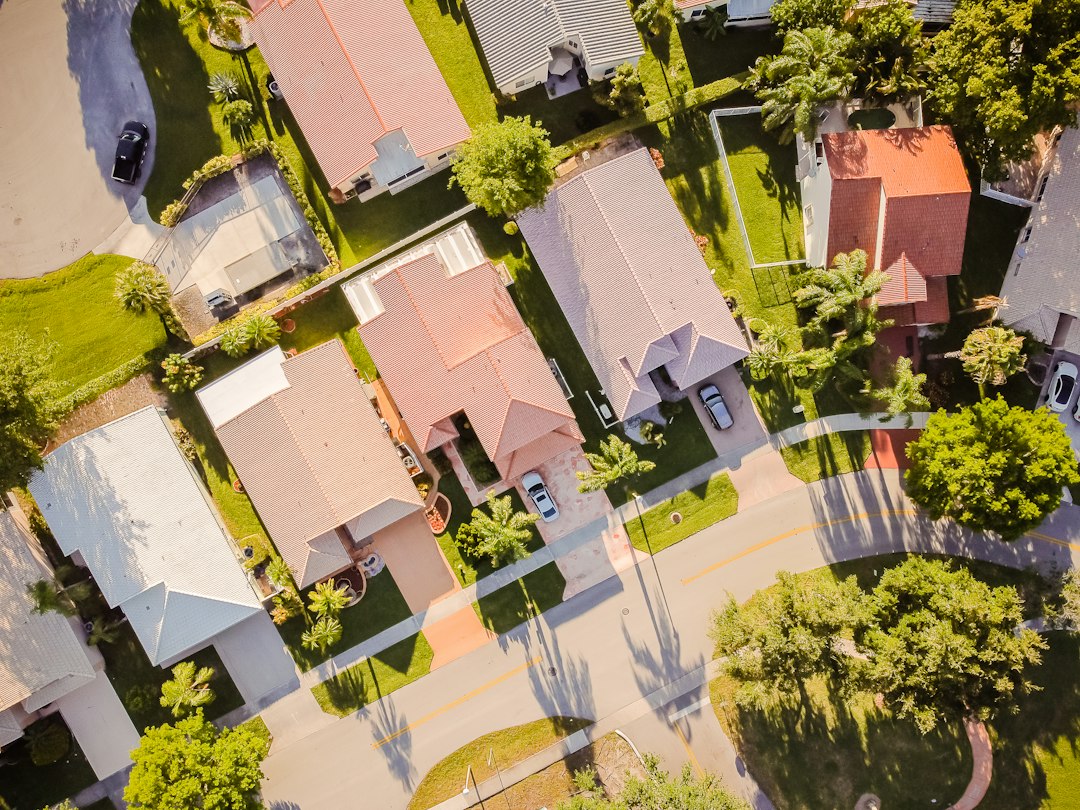 Overhead view of homes, driveways, lawns, and leafy trees in a residential neighborhood.